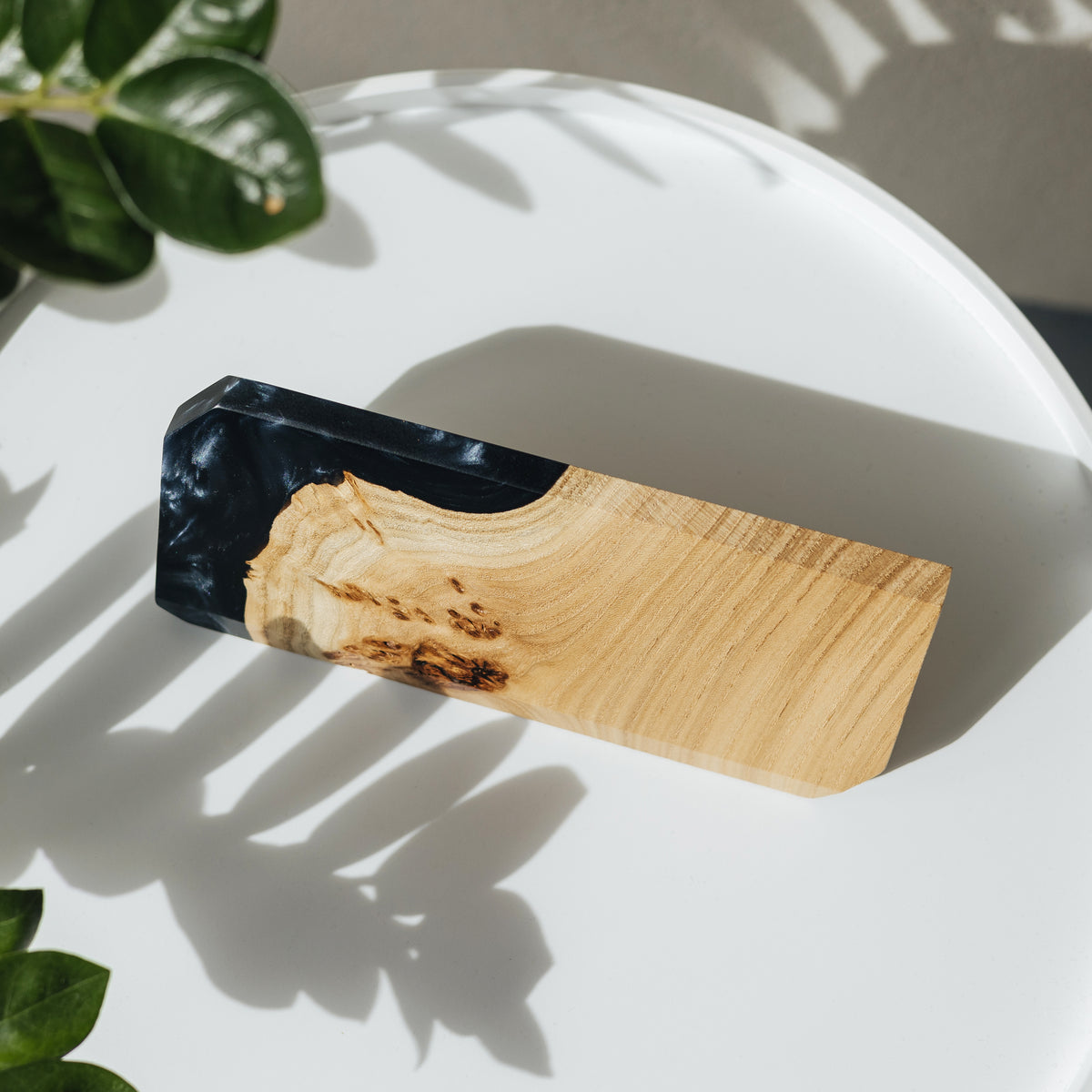 MODERN name plate in black epoxy and elm burl lying on a white round table in dappled leaf shadows