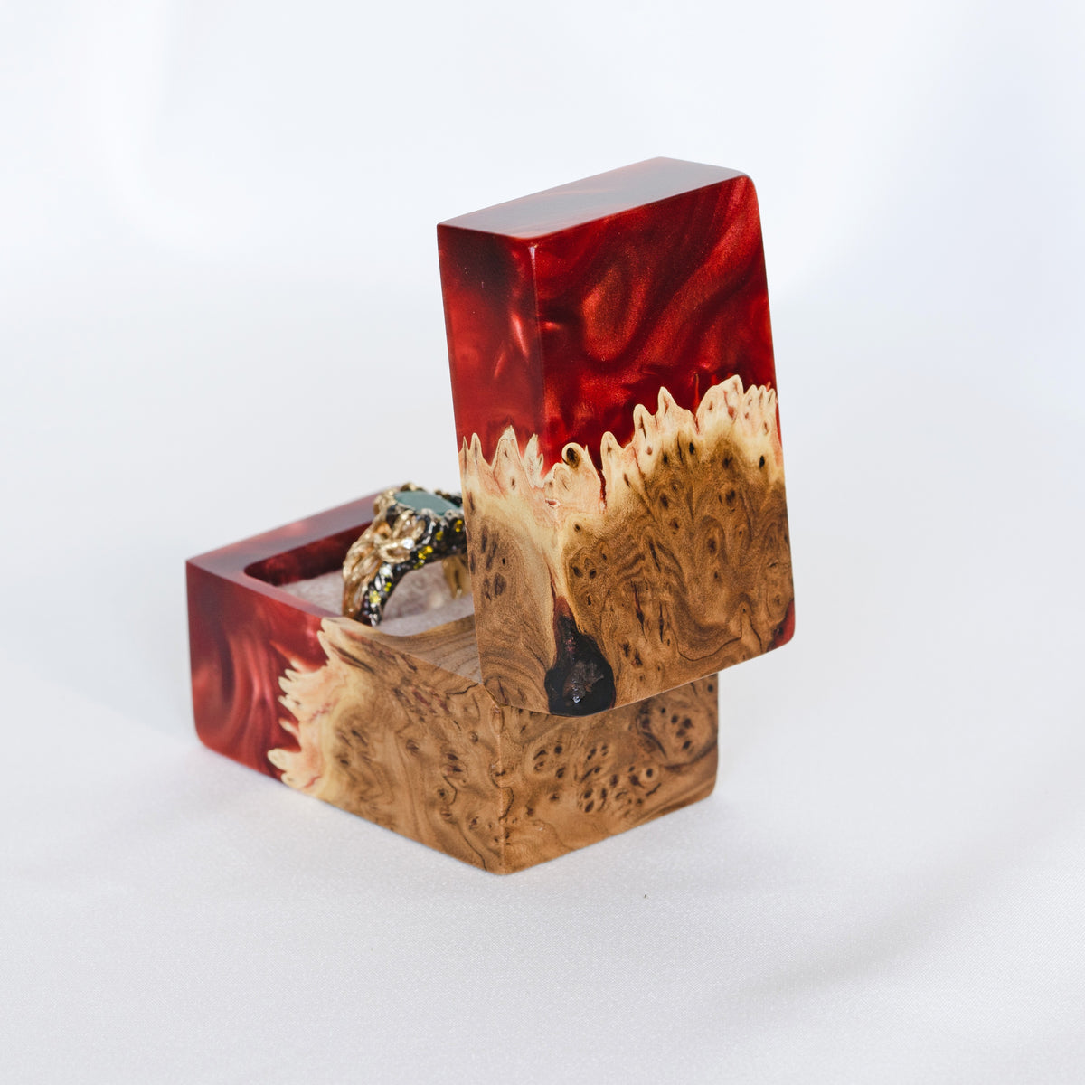 Back of the open ruby epoxy engagement ring box, elm burl lid raised beside an ornate gemstone ring