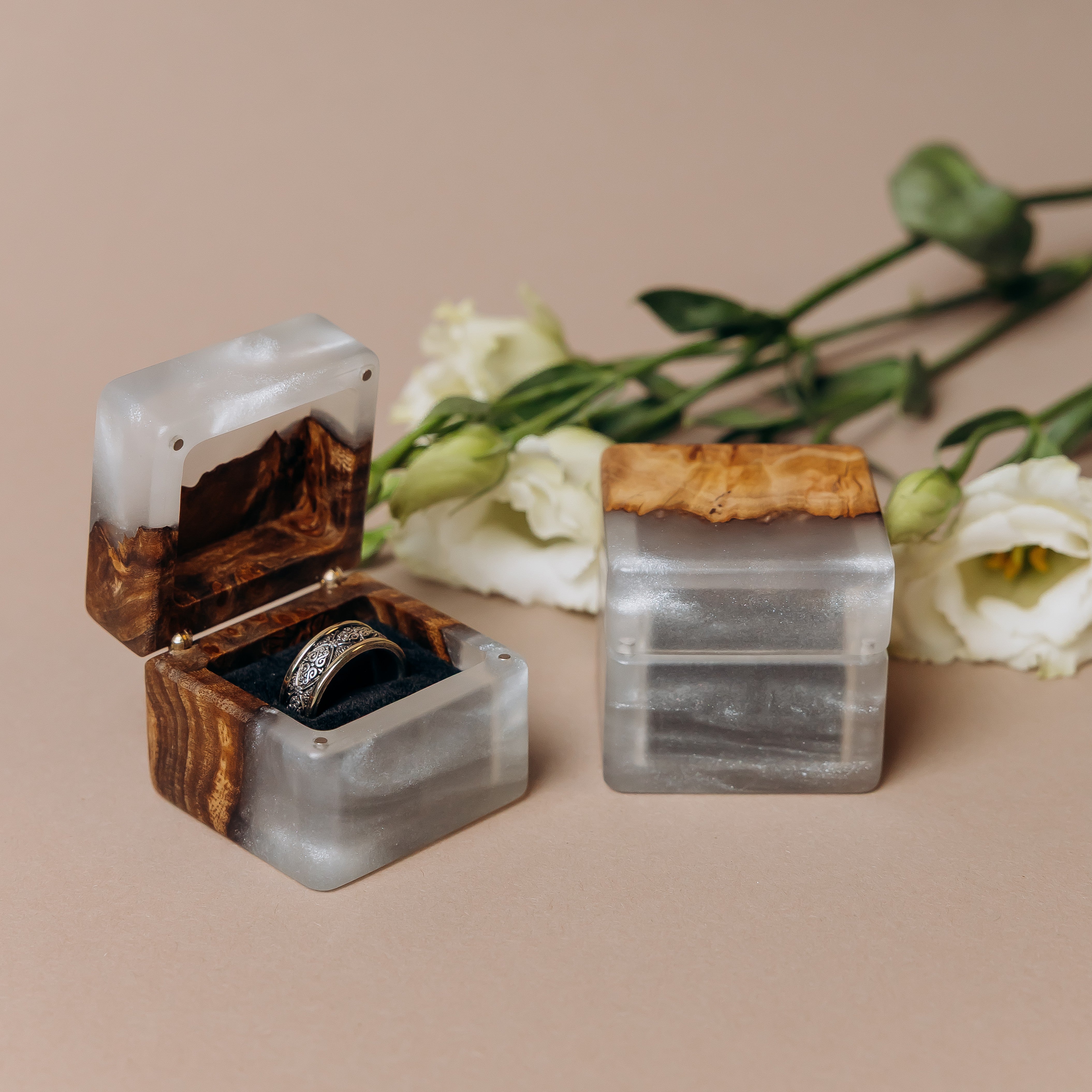 Platinum epoxy elm ring box open on a beige backdrop with white lisianthus behind it
