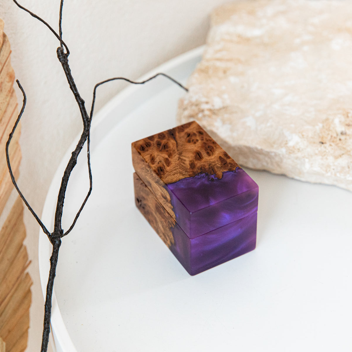 Closed purple epoxy and elm burl ring box on a white tray next to a stone and a dark branch