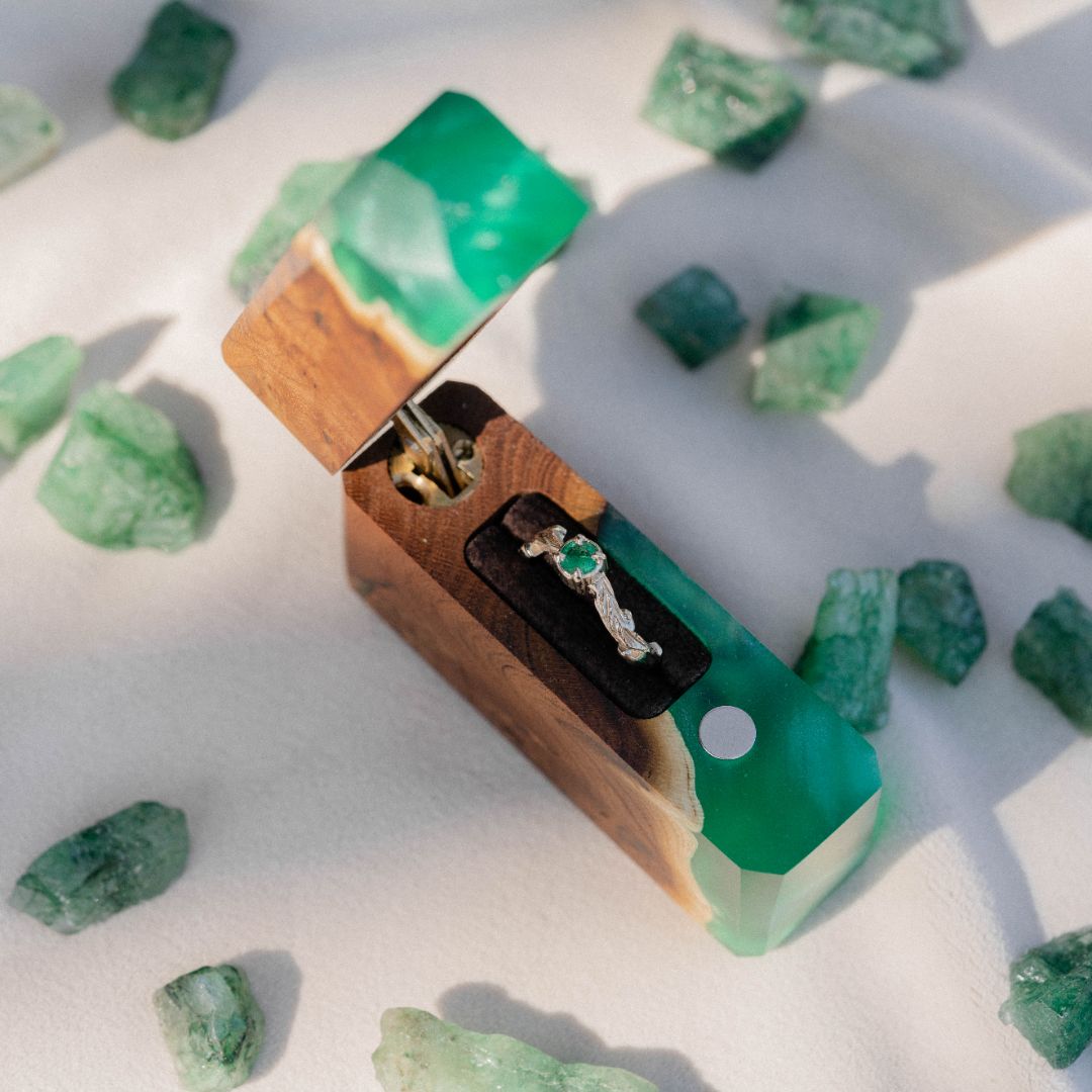 Elegant open green epoxy and elm wood proposal ring box on a white background with decorative stones