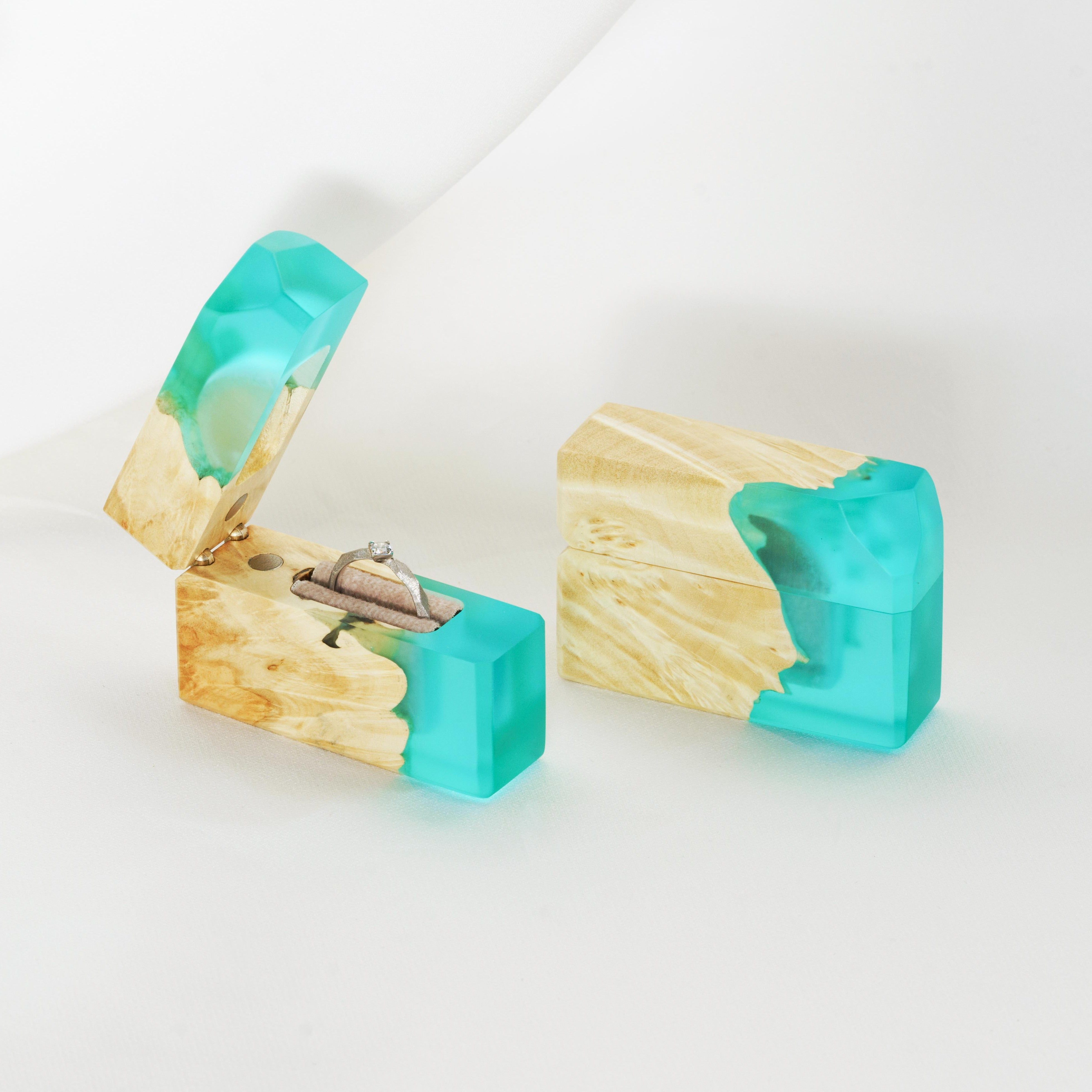 Luxury aqua blue epoxy and maple wood proposal ring box displayed open on a white fabric background
