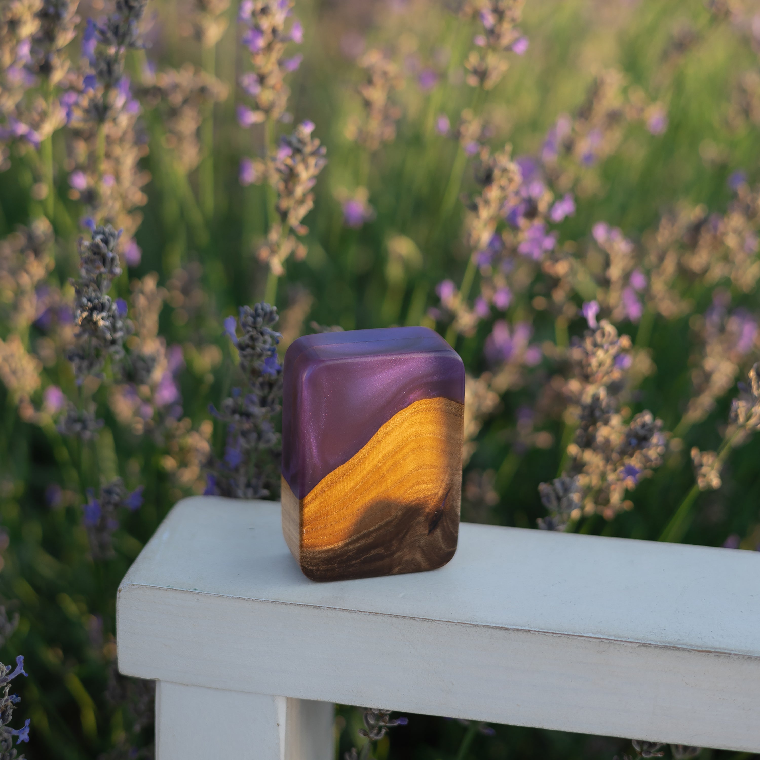 Closed purple epoxy and elm wood engagement ring box displayed in a garden setting
