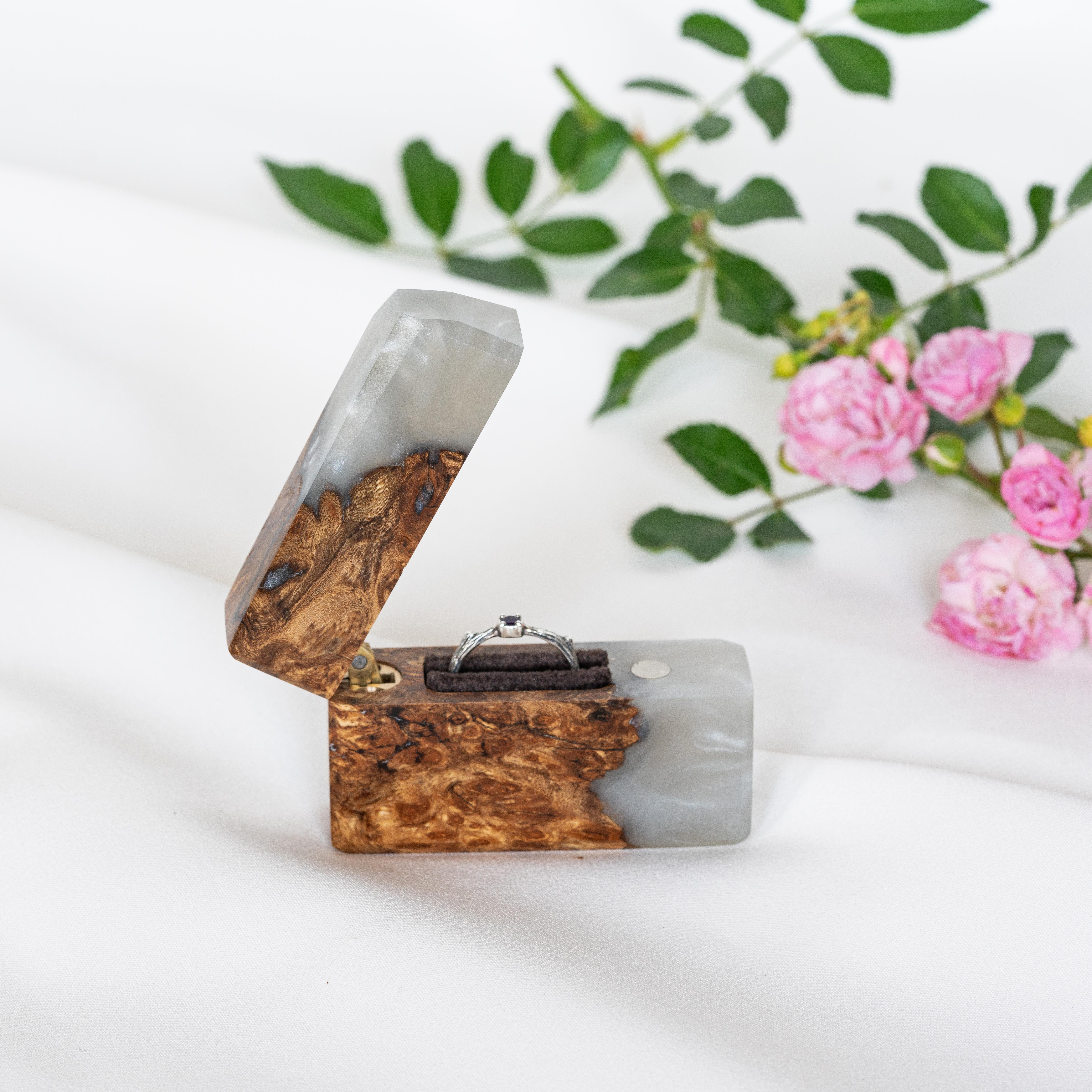 Open engagement ring box handcrafted from platinum epoxy and elm wood with pink flowers in the background