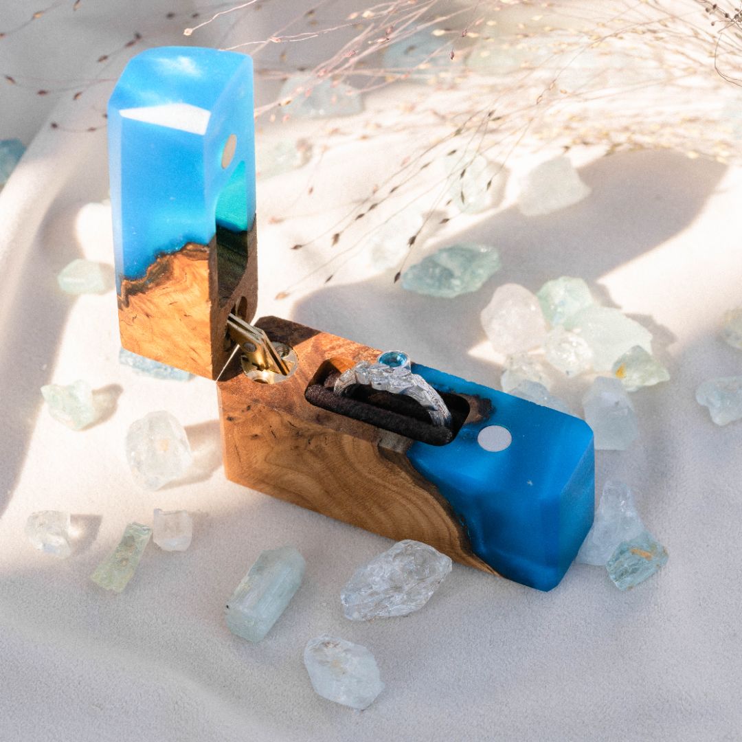 Luxury blue epoxy and elm wood proposal ring box displayed open on decorative crystal stones