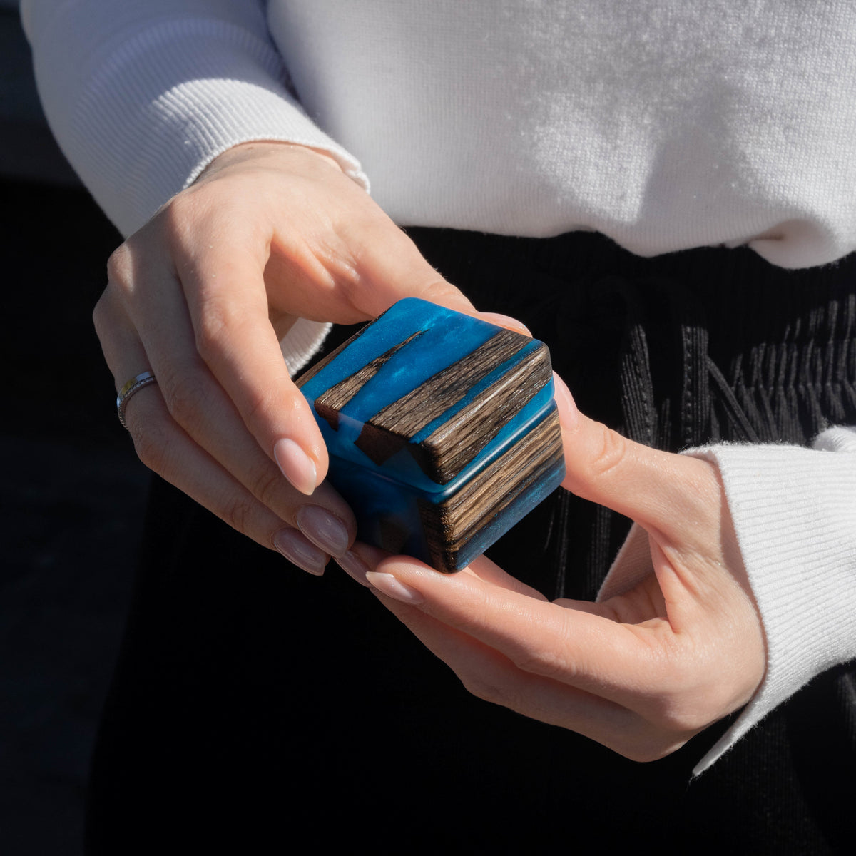 Hands holding the closed blue epoxy and bog oak engagement ring box before a proposal