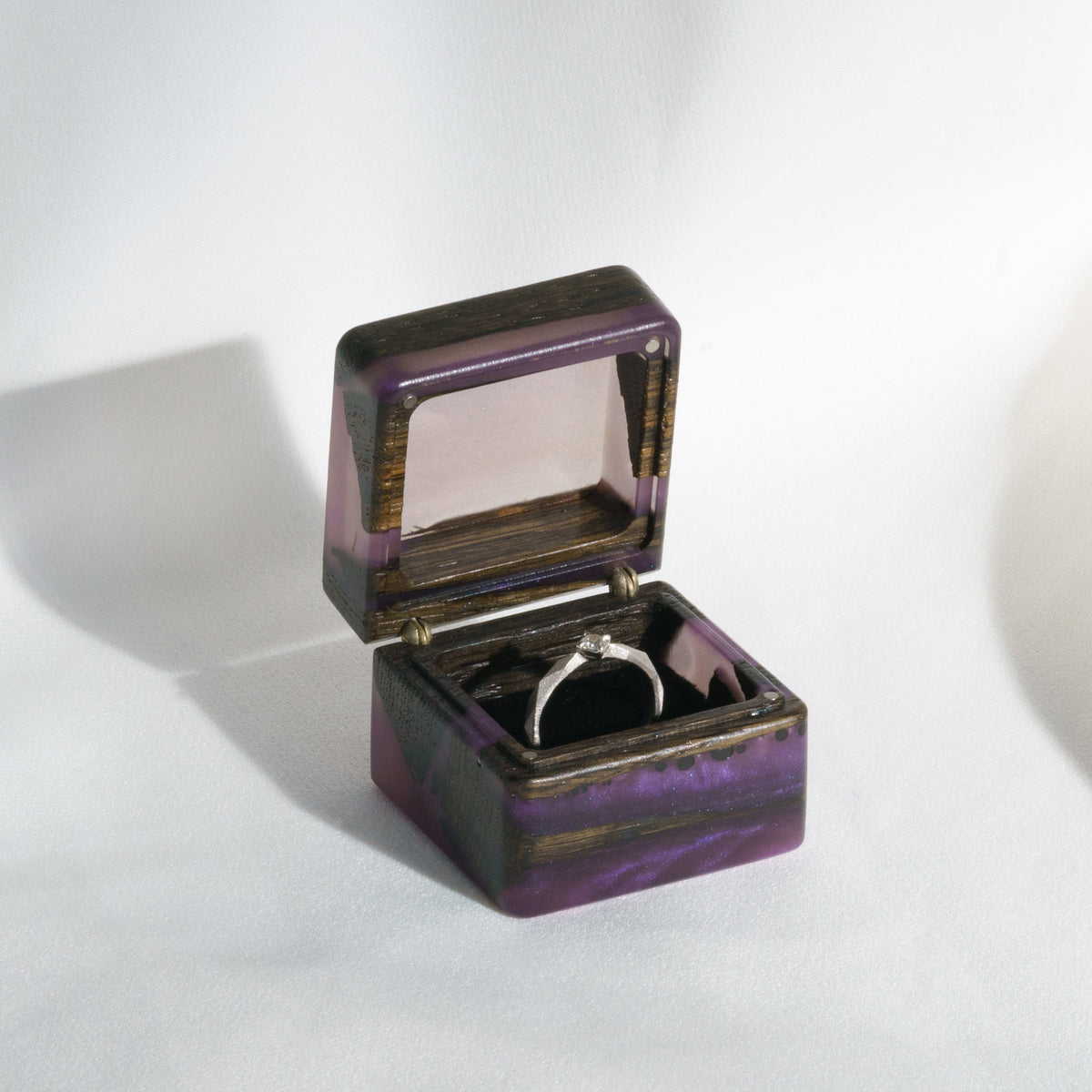 Open purple epoxy proposal ring box with a diamond ring resting on the black pillow