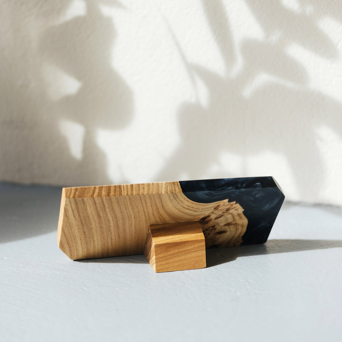 Back of the black epoxy and elm name plate with its wooden support foot, leaf shadows on the wall