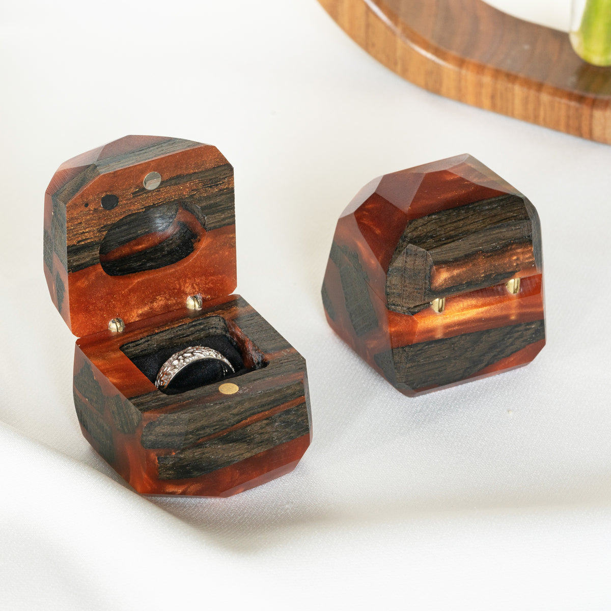 Close-up of a stone-set band in the open amber box, the closed box beside it showing brass hinges
