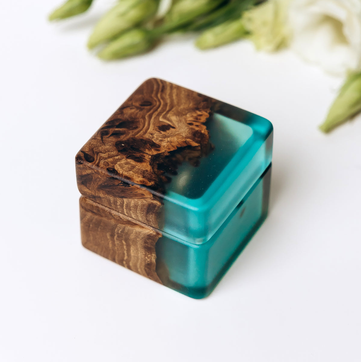 Closed wooden ring box seen from above, elm burl lid meeting the aqua blue epoxy body