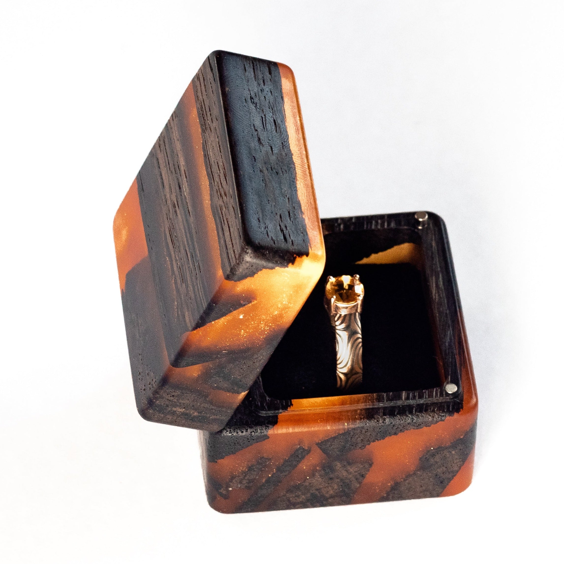 Angled side view of the open amber epoxy and bog oak wood proposal ring box with geometric wood grain