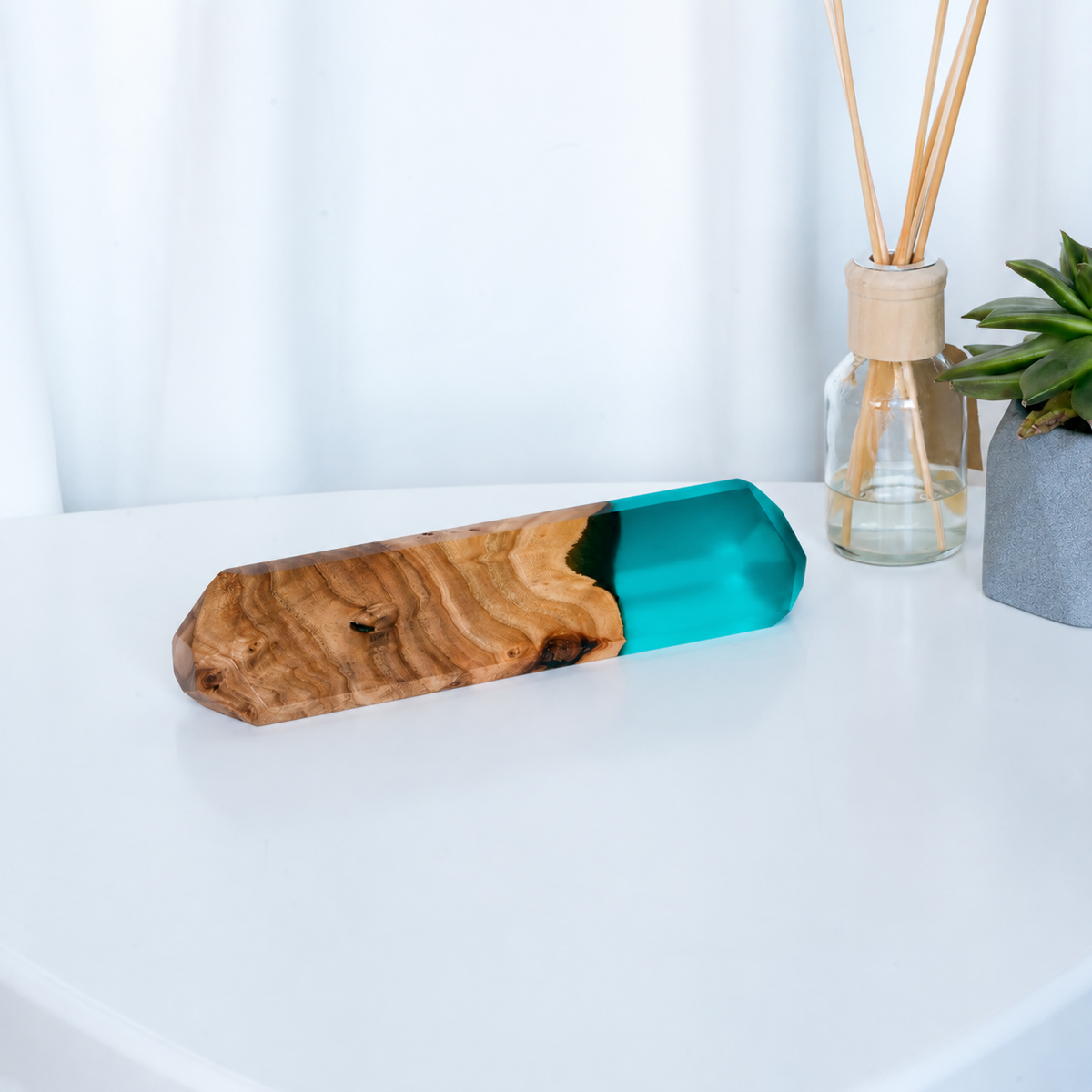 Faceted IDENTITY name plate in aqua blue epoxy and elm burl on a white desk beside a reed diffuser