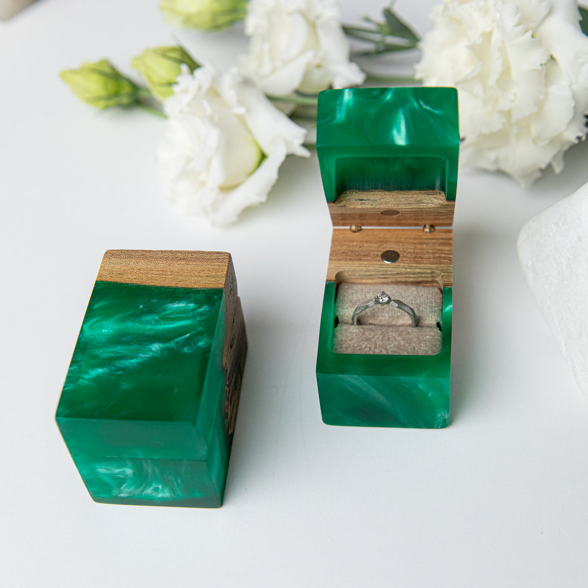 Open and closed green epoxy CHORD boxes with a solitaire ring among white lisianthus