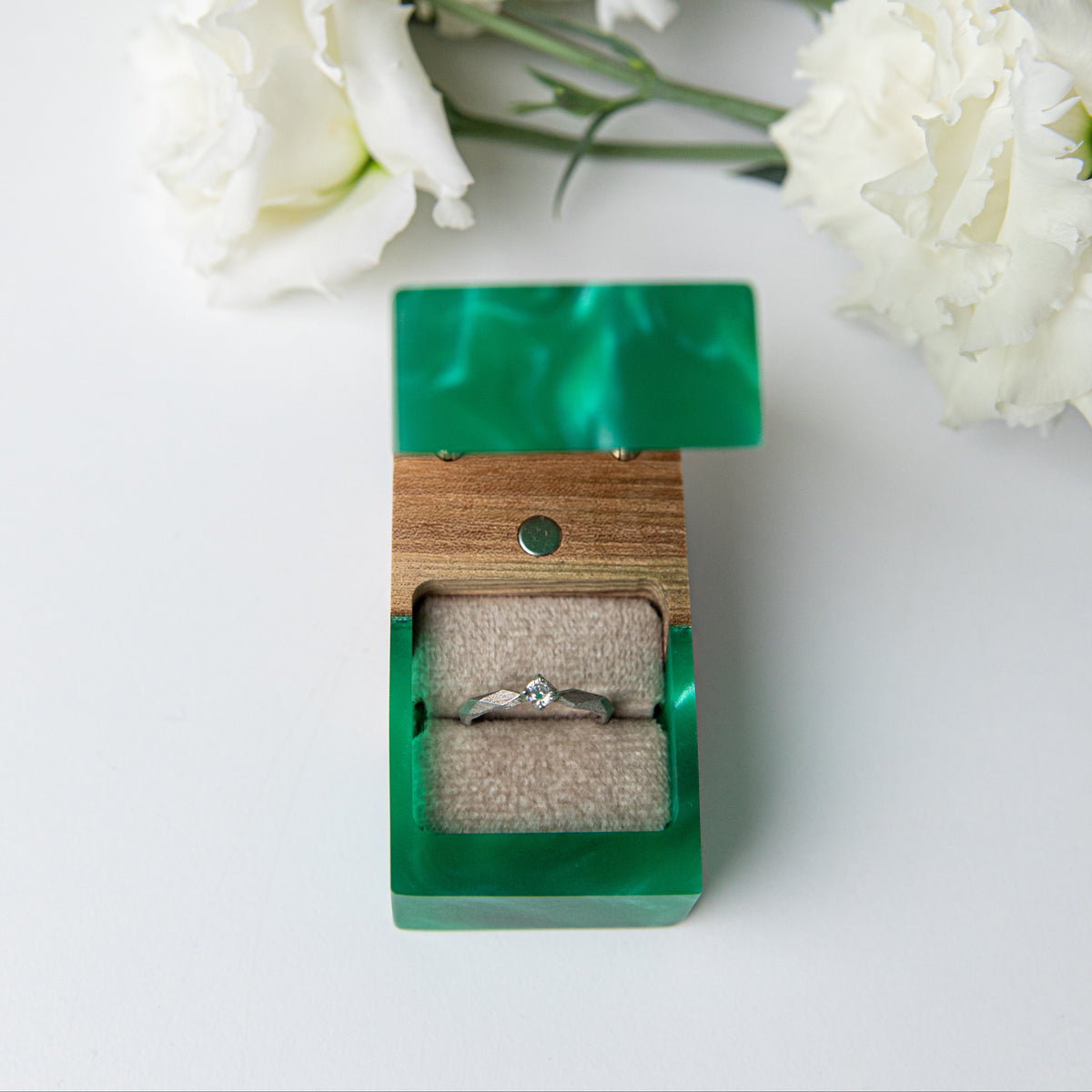 Solitaire ring framed by the open lid of the green and elm box, white lisianthus above