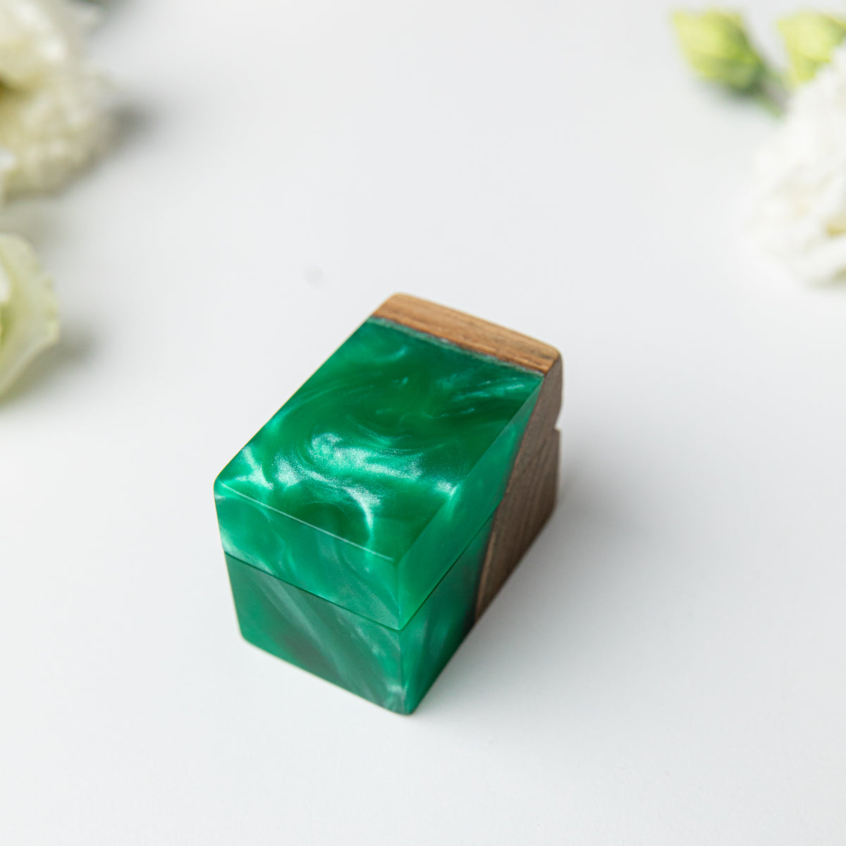 Closed green epoxy and elm ring box with pearly resin swirls, white flowers in the background