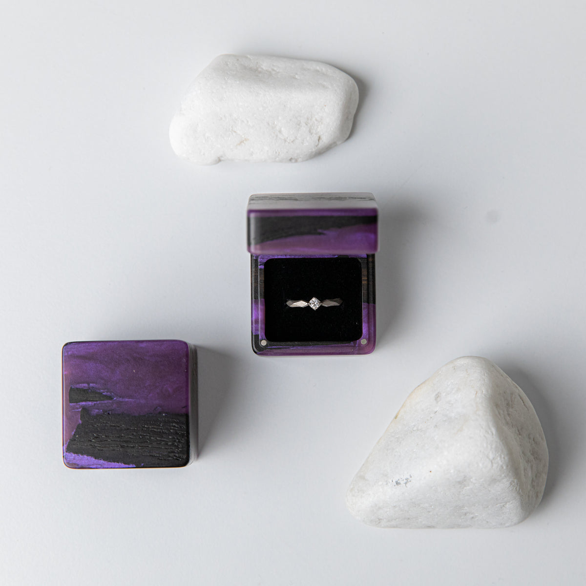 Purple epoxy and bog oak proposal ring box open with a solitaire ring, white stones around it
