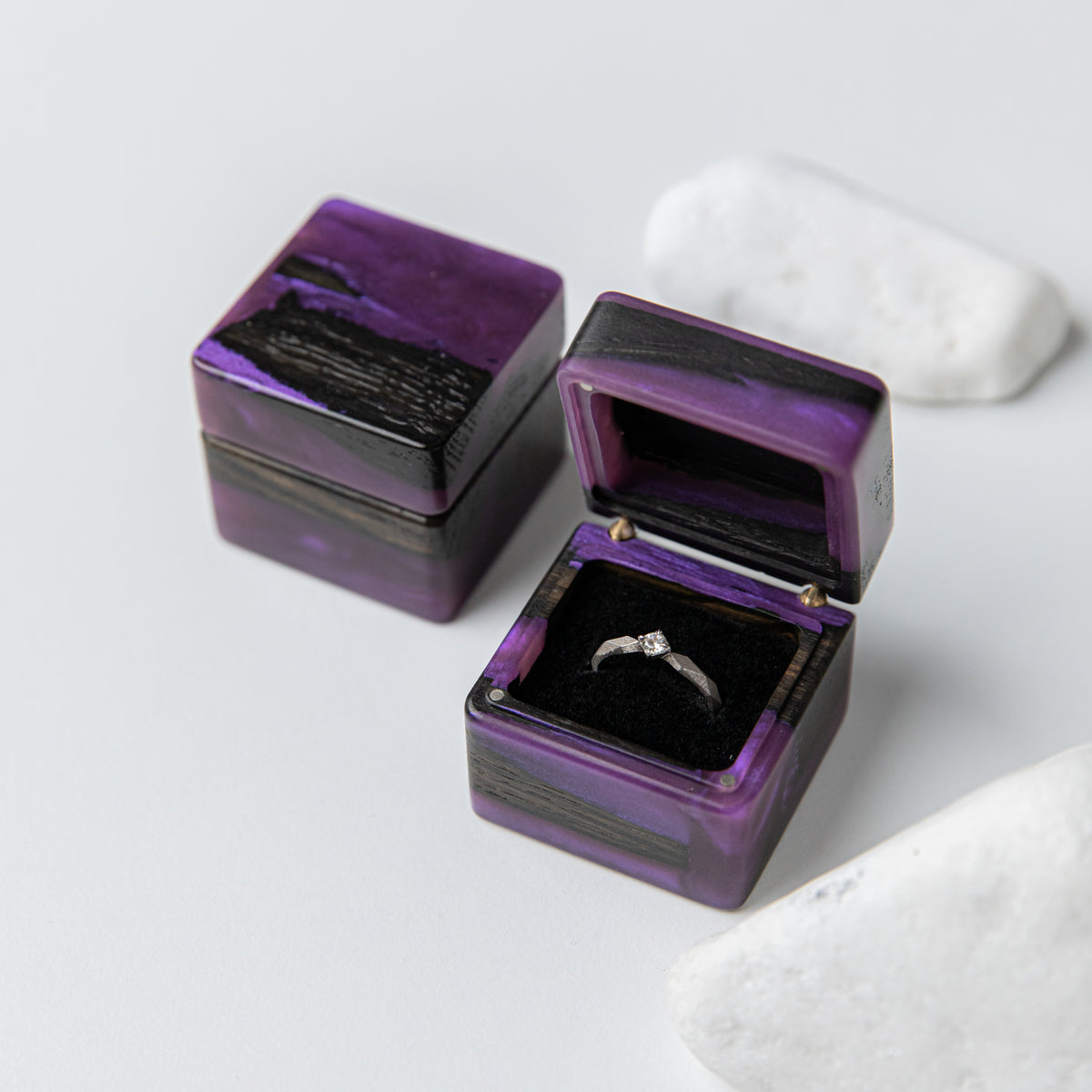 Two purple epoxy bog oak ring boxes, one closed and one open holding an engagement ring