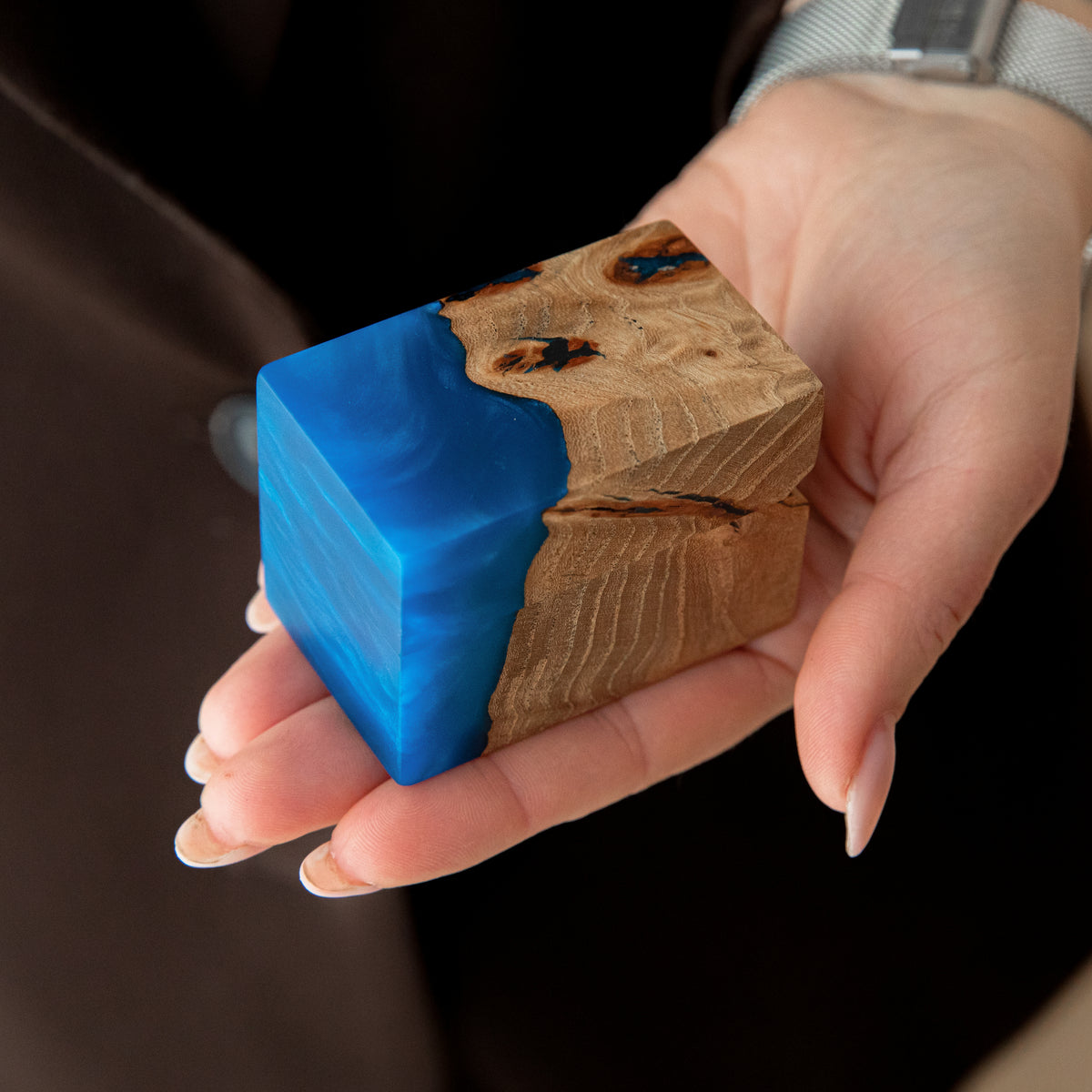 Closed blue epoxy and elm burl ring box resting on an open palm to show its size
