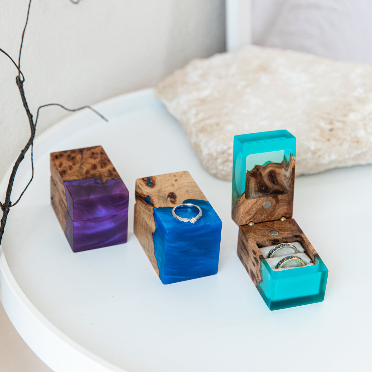 Open aqua blue double ring box with two bands beside closed purple and blue ring boxes on a white tray