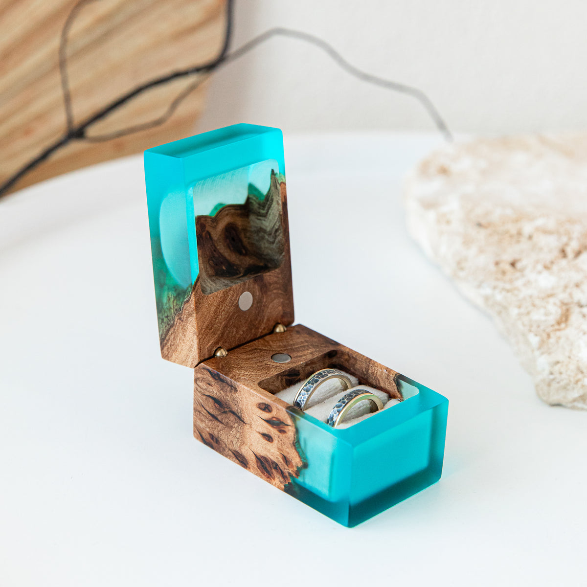 Lid raised on the aqua blue CHORD box, showing elm burl inside and two rings in soft slots