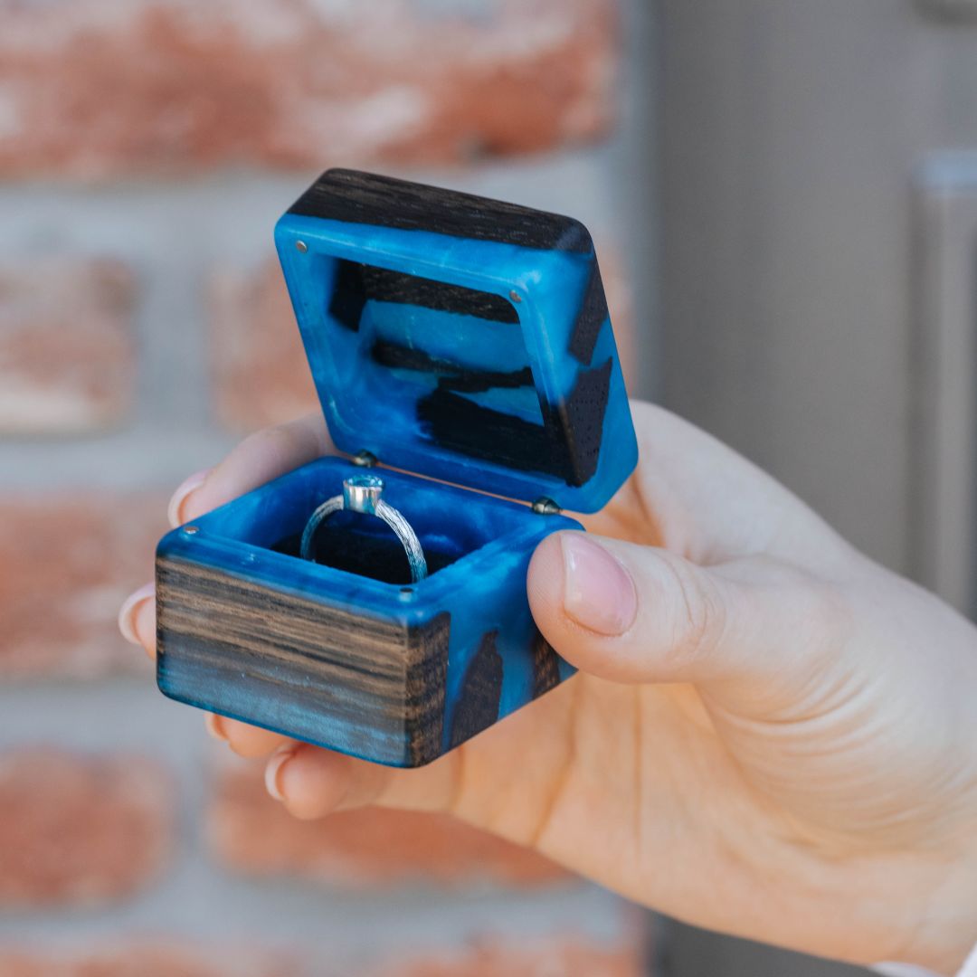 Blue epoxy and bog oak wood engagement ring box held in hand to showcase its size and craftsmanship
