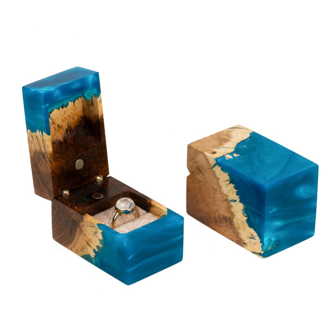 Open and closed blue epoxy and elm wood engagement ring boxes displayed together on a white background